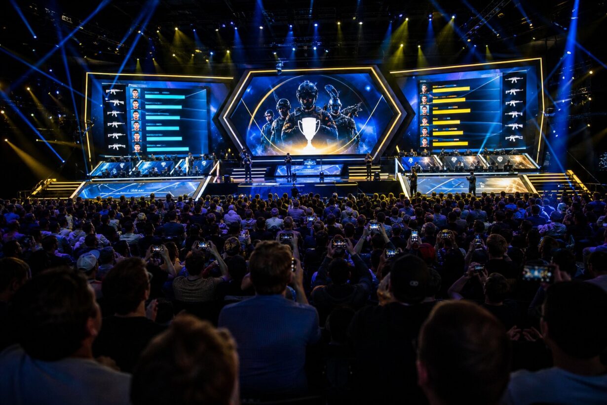 Large esports arena crowd facing a lit stage with giant screens displaying player stats and a trophy graphic during a Counter-Strike tournament