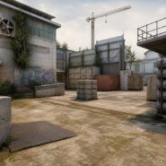 An industrial courtyard in a video game map with crates, barrels, graffiti, and a construction crane in the background
